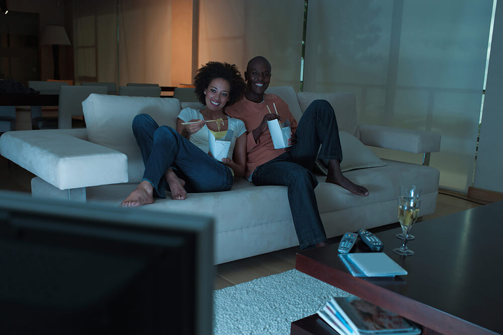 Couple eating Chinese food together on the couch, happily