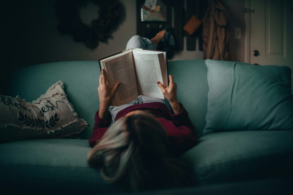 Aerial view of a dark-haired women reading a book on a hunter green couch.